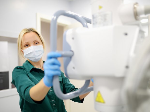 a radiology worker adjusts the imagining unit of an x-ray machine