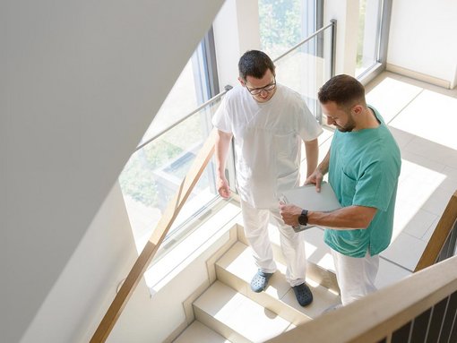 zwei Pfleger stehen an einer Treppe und schauen auf ein Klemmbrett
